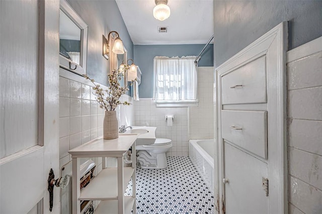 bathroom with visible vents, a wainscoted wall, toilet, tile walls, and washtub / shower combination