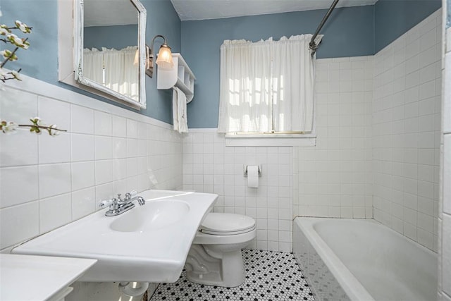 bathroom with tile patterned flooring, toilet, wainscoting, tile walls, and a sink