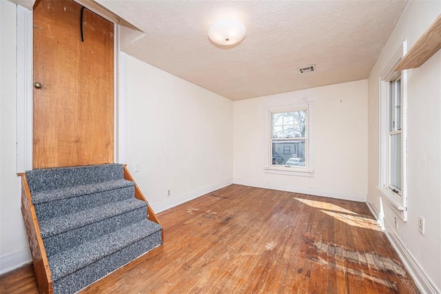 spare room featuring hardwood / wood-style flooring, baseboards, visible vents, and a textured ceiling