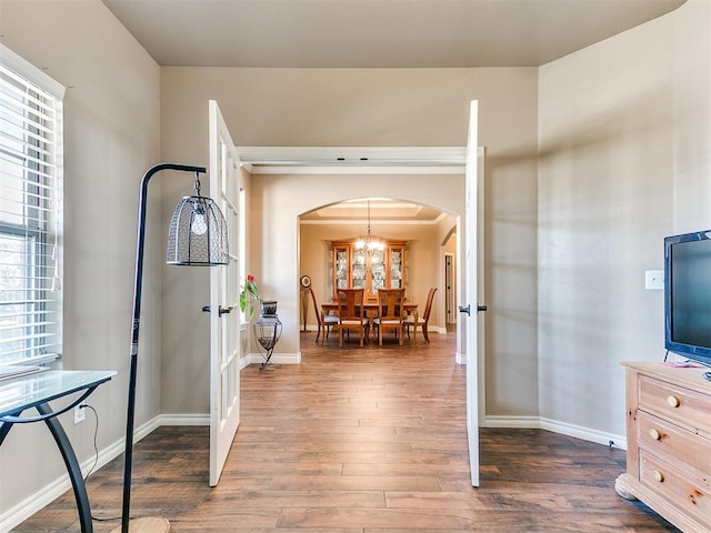 foyer featuring dark wood-type flooring, baseboards, arched walkways, and a chandelier