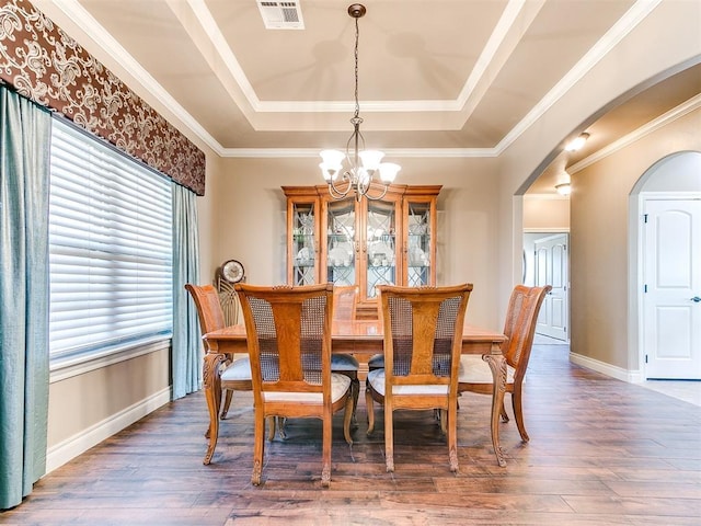 dining space with visible vents, a tray ceiling, wood finished floors, arched walkways, and a chandelier