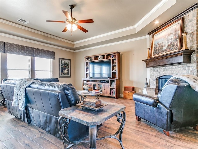 living room with a fireplace, a raised ceiling, wood finished floors, and visible vents