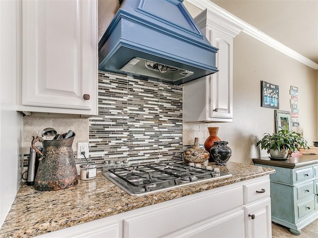 kitchen with tasteful backsplash, crown molding, custom range hood, stainless steel gas stovetop, and white cabinetry