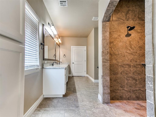 full bath with visible vents, baseboards, vanity, and a tile shower