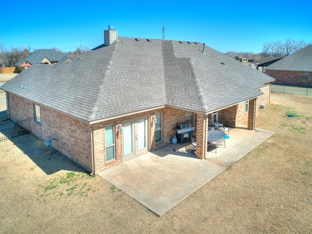 back of property with brick siding, roof with shingles, a chimney, a yard, and a patio area