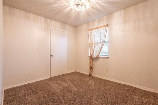 carpeted spare room featuring baseboards, a textured ceiling, an inviting chandelier, and a textured wall