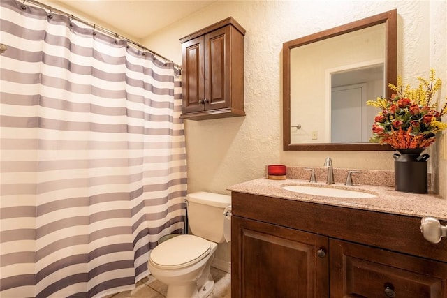 full bath with toilet, vanity, and a textured wall