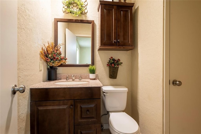 bathroom with toilet, vanity, and a textured wall