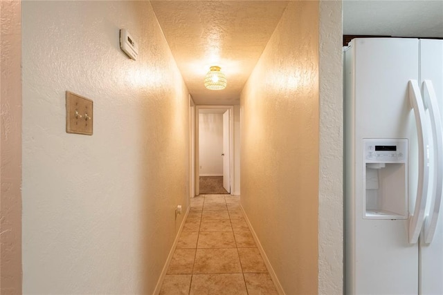 hallway with light tile patterned floors, a textured ceiling, and a textured wall