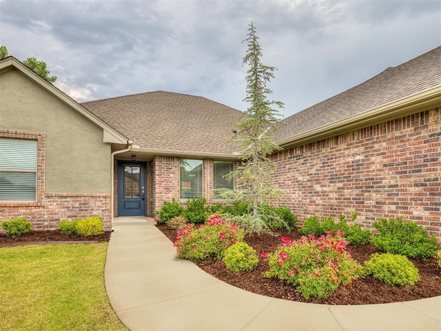 entrance to property featuring stucco siding, brick siding, and a shingled roof