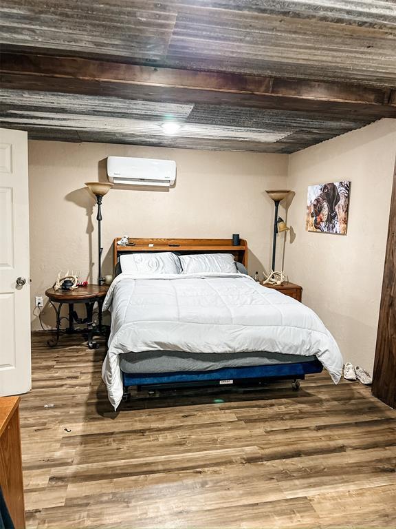 bedroom featuring an AC wall unit, wood finished floors, and beam ceiling