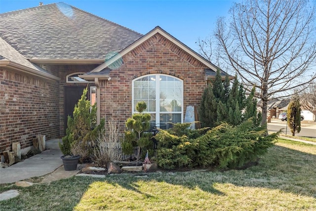 view of property exterior featuring brick siding, roof with shingles, and a lawn