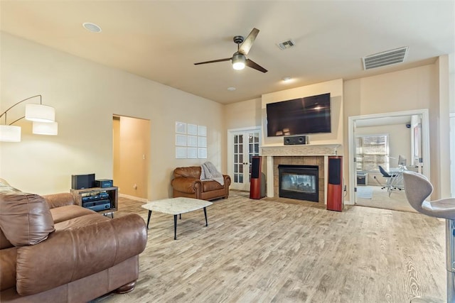 living room with a tiled fireplace, wood finished floors, visible vents, and ceiling fan