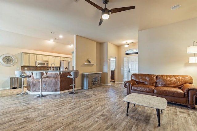 living room featuring ceiling fan, baseboards, and light wood-style flooring