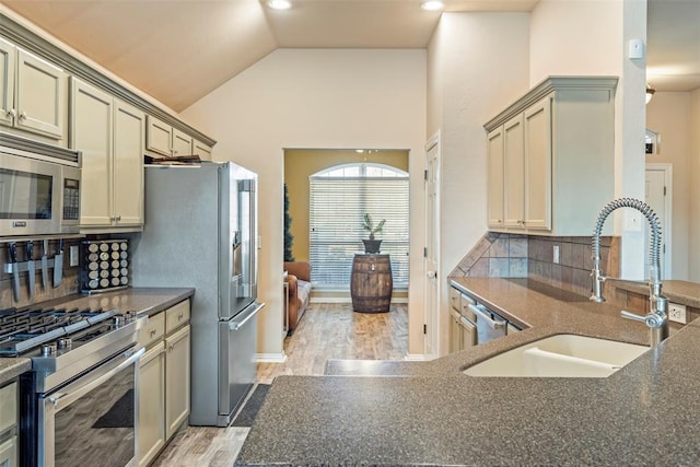 kitchen with light wood finished floors, a sink, stainless steel appliances, vaulted ceiling, and tasteful backsplash