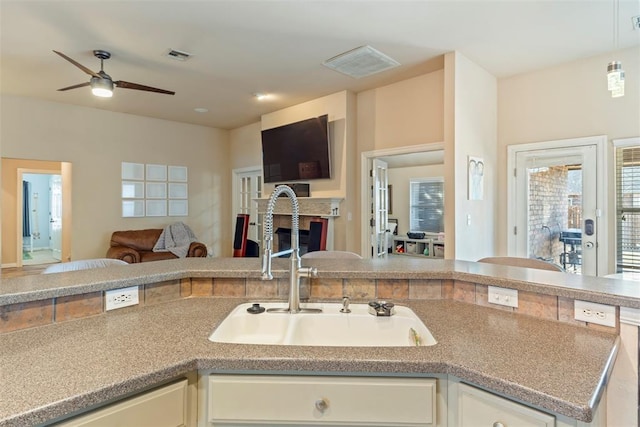 kitchen with visible vents, a sink, open floor plan, white cabinetry, and a fireplace