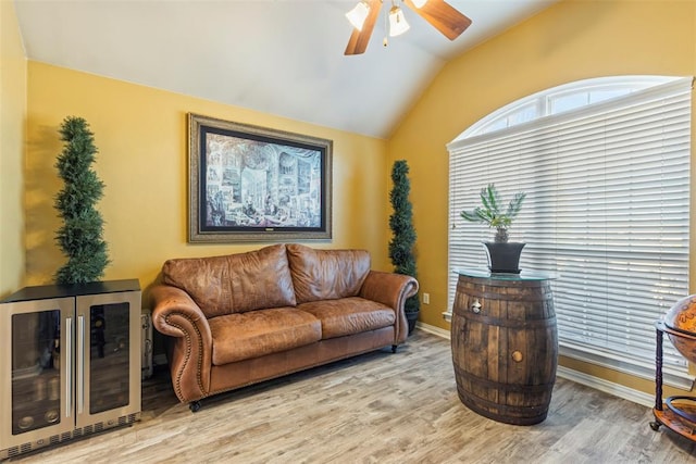 living area featuring light wood-type flooring, a ceiling fan, wine cooler, baseboards, and vaulted ceiling