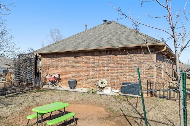 rear view of house with a patio, brick siding, a shingled roof, and fence