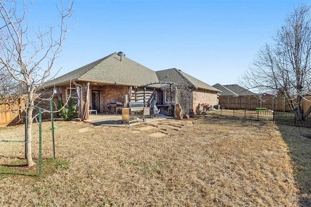 rear view of house featuring a lawn, a fenced backyard, roof with shingles, brick siding, and a patio area