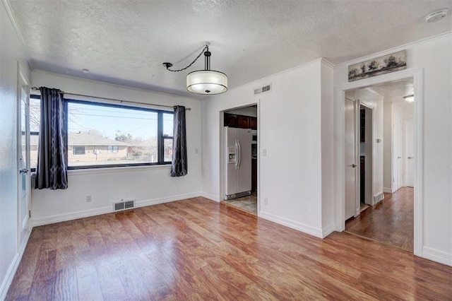 empty room featuring light wood-type flooring, visible vents, a textured ceiling, and crown molding