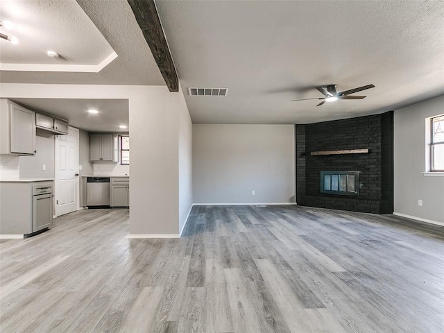 unfurnished living room featuring light wood-style flooring, a fireplace, visible vents, and a textured ceiling