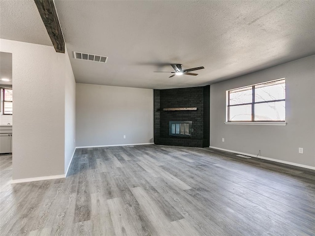 unfurnished living room with visible vents, ceiling fan, a fireplace, wood finished floors, and a textured ceiling