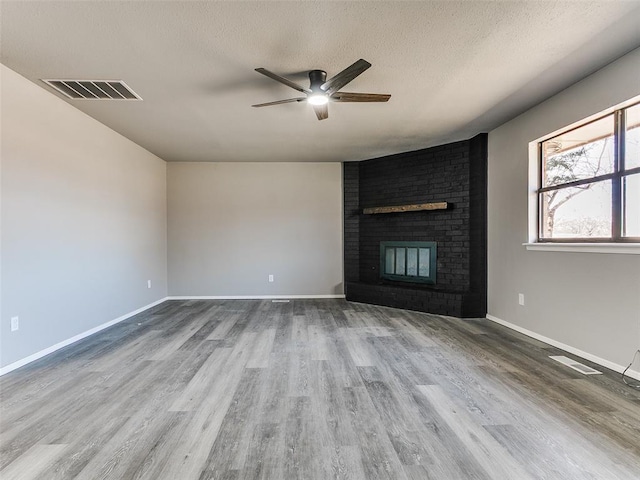 unfurnished living room with a fireplace, wood finished floors, visible vents, and a textured ceiling