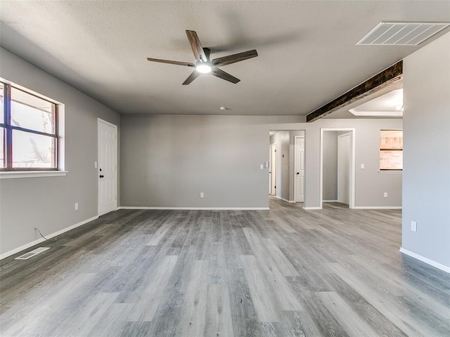 unfurnished living room featuring a textured ceiling, wood finished floors, visible vents, and baseboards