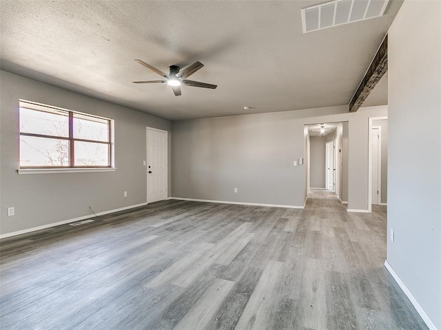 unfurnished room featuring a ceiling fan, baseboards, wood finished floors, visible vents, and a textured ceiling