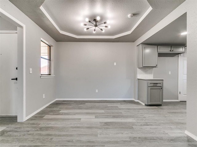 unfurnished living room featuring light wood-style flooring, a tray ceiling, a textured ceiling, an inviting chandelier, and baseboards