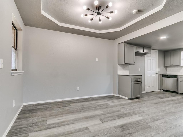 kitchen with decorative backsplash, a raised ceiling, stainless steel dishwasher, and gray cabinets