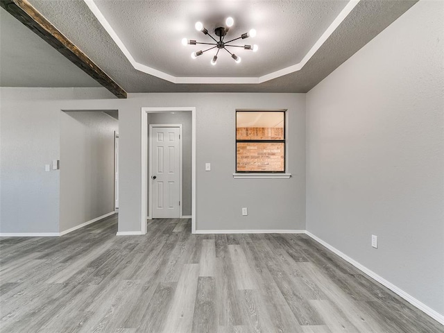 spare room with a raised ceiling, wood finished floors, baseboards, and a textured ceiling