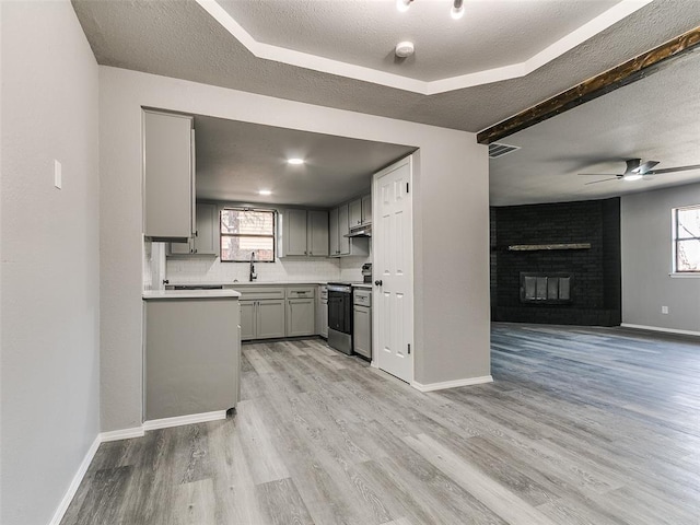 kitchen with gray cabinets, a sink, open floor plan, stainless steel range with electric cooktop, and light wood-style floors