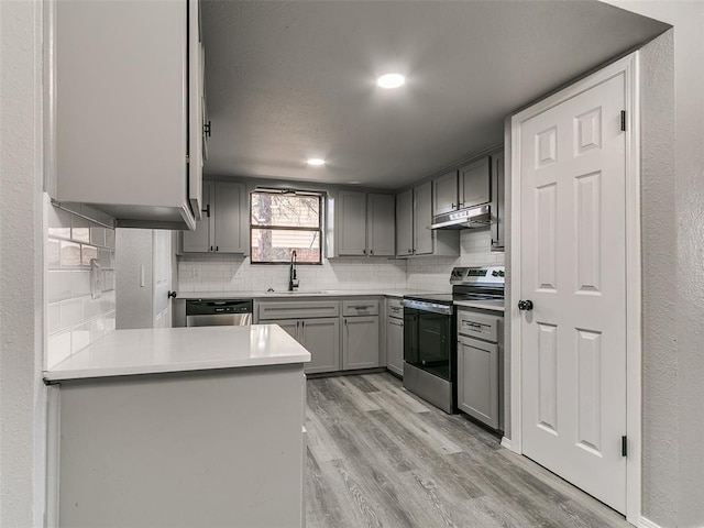 kitchen with gray cabinets, stainless steel appliances, under cabinet range hood, light wood-type flooring, and backsplash