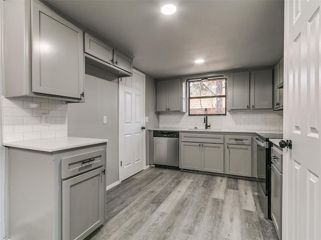 kitchen featuring light wood-style flooring, gray cabinets, a sink, light countertops, and appliances with stainless steel finishes