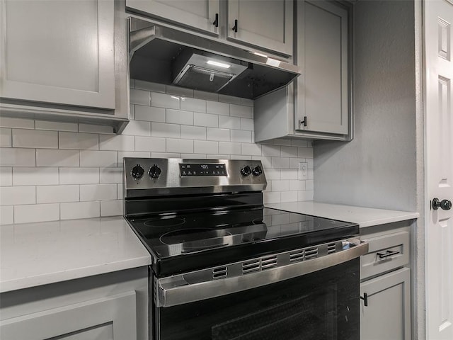 kitchen featuring under cabinet range hood, gray cabinetry, stainless steel electric range oven, and tasteful backsplash