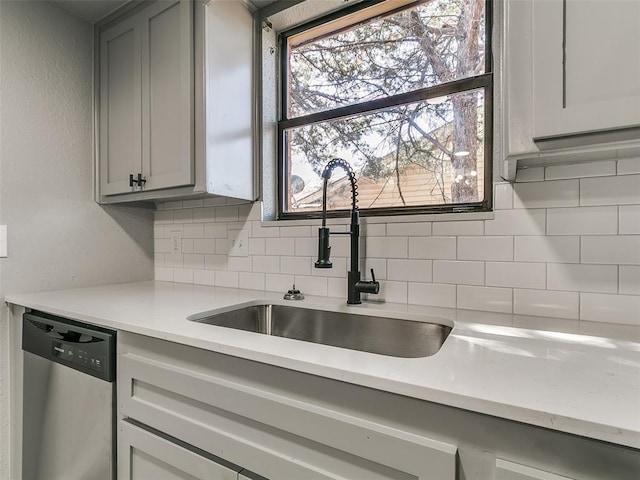 kitchen with stainless steel dishwasher, gray cabinetry, tasteful backsplash, and a sink