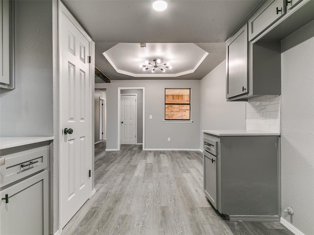 interior space with a tray ceiling, baseboards, and light wood finished floors