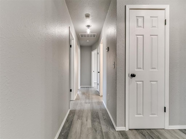 hall with visible vents, a textured ceiling, wood finished floors, baseboards, and a textured wall