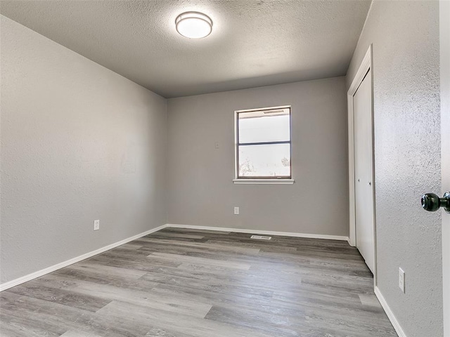 unfurnished bedroom featuring a textured ceiling, wood finished floors, a closet, baseboards, and a textured wall