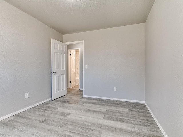 spare room featuring light wood-type flooring, baseboards, and a textured ceiling