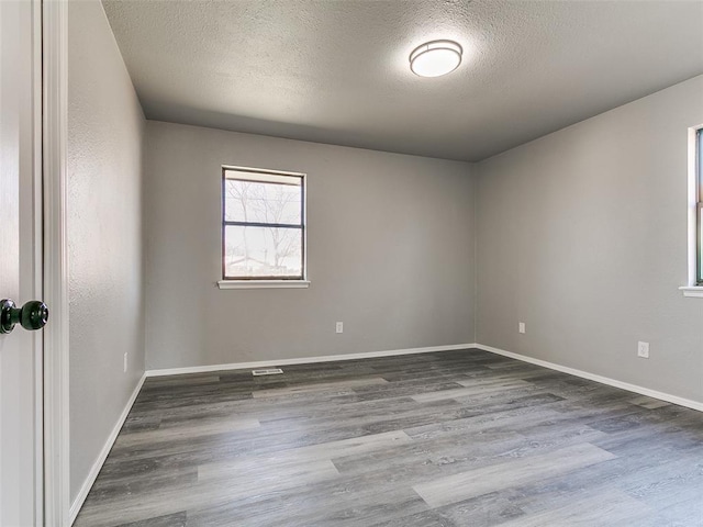 empty room with baseboards, a textured ceiling, and wood finished floors