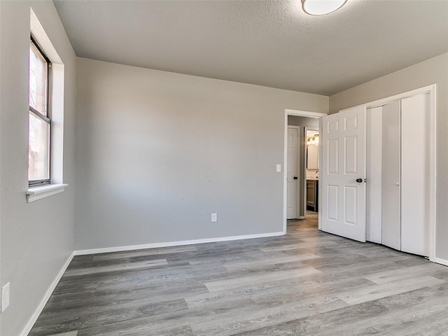 unfurnished bedroom with a closet, a textured ceiling, baseboards, and wood finished floors