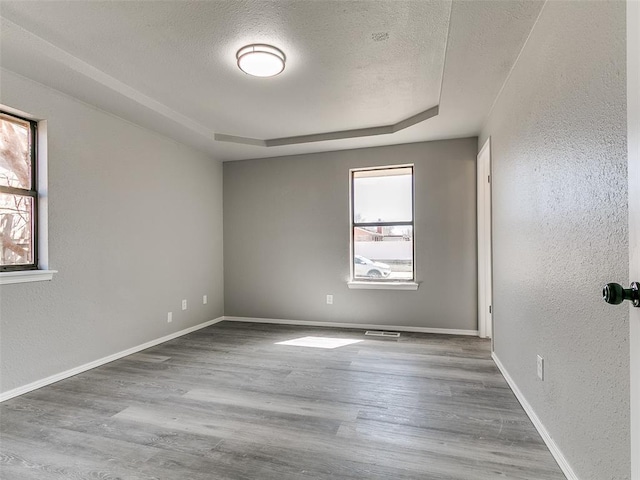 spare room with visible vents, baseboards, wood finished floors, a textured ceiling, and a raised ceiling