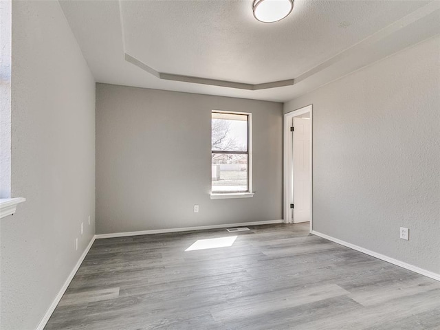 empty room featuring visible vents, a textured ceiling, wood finished floors, baseboards, and a raised ceiling