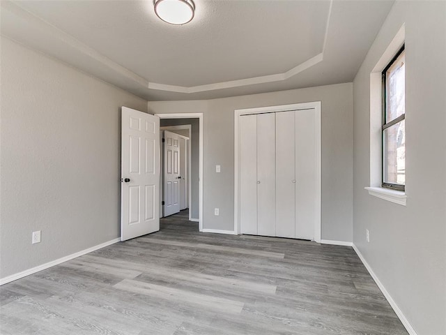 unfurnished bedroom featuring a tray ceiling, wood finished floors, baseboards, and a closet