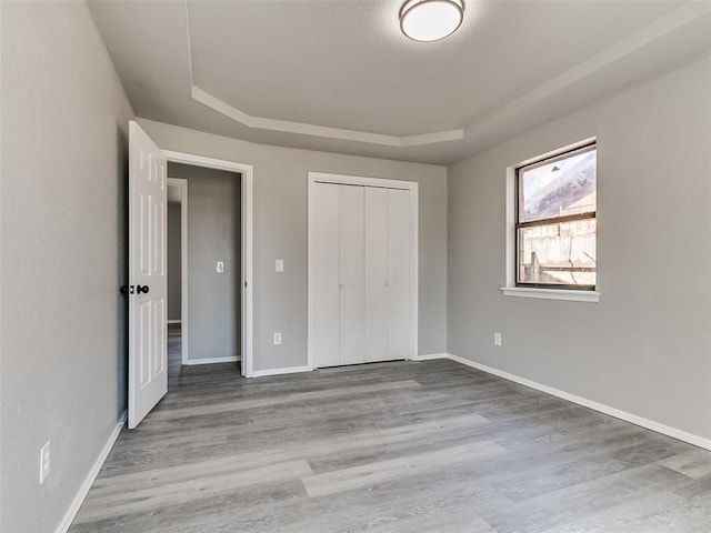 unfurnished bedroom with a closet, baseboards, a tray ceiling, and wood finished floors