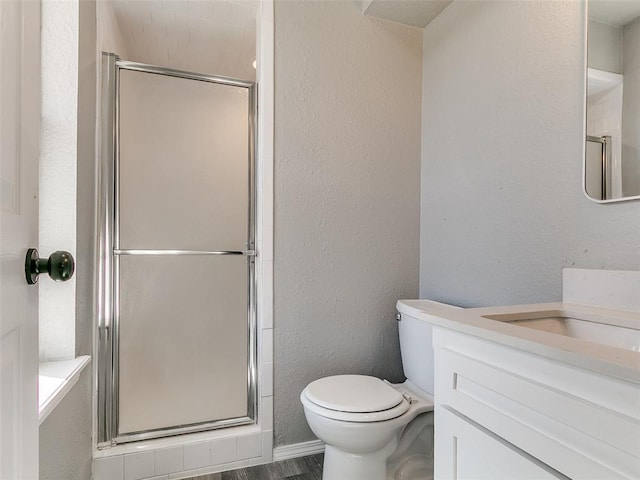 bathroom with a stall shower, toilet, vanity, and a textured wall