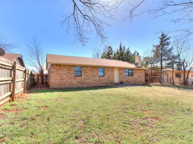 rear view of property with brick siding, a yard, a chimney, and a fenced backyard