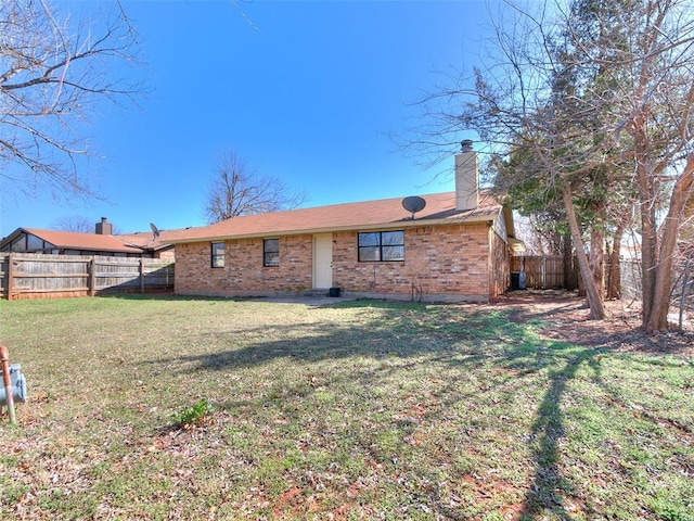 back of house with brick siding, a chimney, fence private yard, and a yard